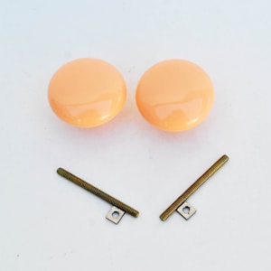 May include: Two peach-colored ceramic knobs with two gold screws and square metal plates.
