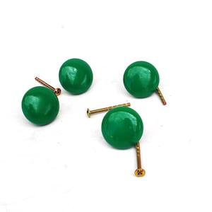 Op de afbeelding: Vier groene, ronde kastknoppen met messing schroeven zijn gerangschikt op een wit oppervlak. De knoppen hebben een glanzende afwerking. Deze decoratieve knoppen zijn geschikt voor meubel- of woondecoratieprojecten.