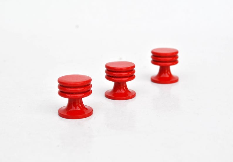 May include: Three small, red, wooden knobs with a round top and a tiered, cylindrical body. The knobs are evenly spaced against a white background. The knobs are likely for furniture or decorative purposes.