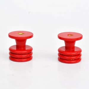 May include: Two red cabinet knobs with a stacked, cylindrical design. Each knob has a flat, circular top and a flared base. The knobs are made of a glossy, solid red material and are set against a white background.
