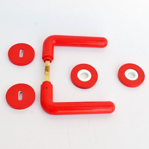 May include: A set of bright red door handles featuring two L-shaped levers connected by a central metal spindle, accompanied by two circular escutcheon plates with vertical keyholes and two circular mounting plates with white centers.