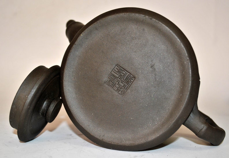 May include: A dark brown ceramic teapot with a lid and a square stamp on the bottom. The stamp reads "製于宜興".
