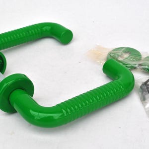 May include: Two bright green door handles with a ridged design, along with mounting hardware. The handles have a curved shape and are made of a glossy material. The hardware includes green washers and an Allen wrench.