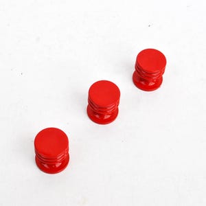 May include: Three small, bright red, cylindrical objects with a rounded top and a grooved base. The objects are evenly spaced against a white background, creating a clean and simple composition. The objects appear to be made of a glossy material.