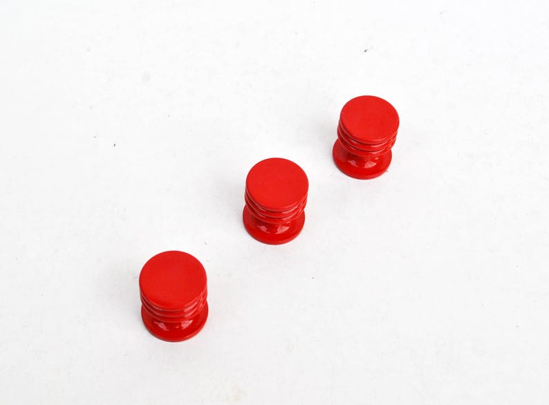 May include: Three small, bright red, cylindrical objects with a rounded top and a grooved base. The objects are evenly spaced against a white background, creating a clean and simple composition. The objects appear to be made of a glossy material.