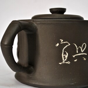 May include: A dark brown ceramic teapot with a lid and a handle. The teapot has white calligraphy on the side.
