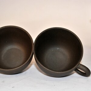 May include: Two brown ceramic teacups with handles, and a matching brown teapot in the background.