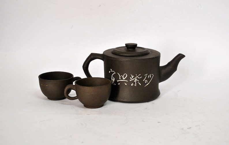 May include: A brown ceramic teapot with a white inscription in Chinese characters, "茶艺",  and two matching brown ceramic teacups.