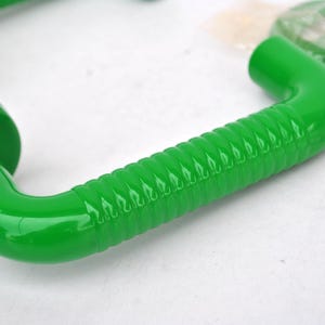 May include: Bright green door handles with a curved design and a ridged grip. The handles have a glossy finish and are likely made of plastic or metal. Hardware for installation is visible in the background.
