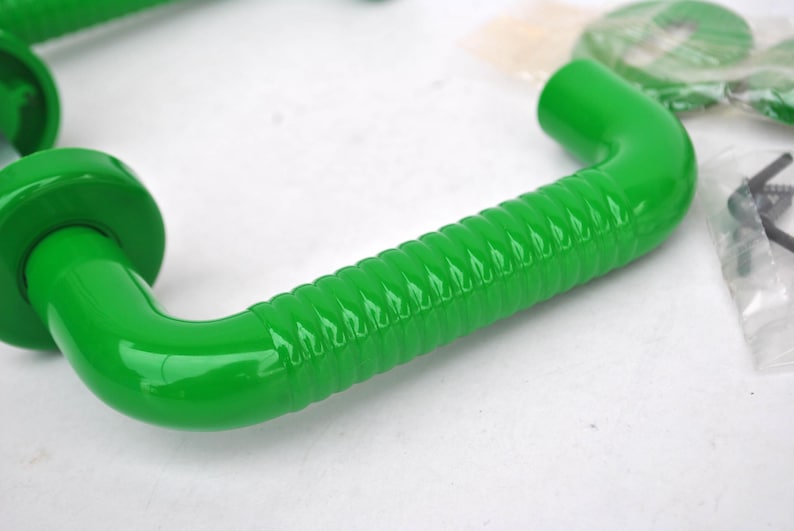 May include: Bright green door handles with a curved design and a ridged grip. The handles have a glossy finish and are likely made of plastic or metal. Hardware for installation is visible in the background.