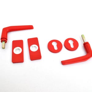 May include: A set of bright red door hardware including two L-shaped handles with metal spindles, two rectangular plates with circular cutouts, and two circular escutcheon plates featuring keyhole openings, all displayed on a plain white background.
