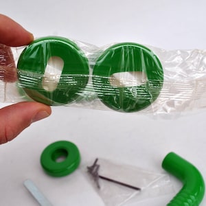 May include: A collection of green plastic parts, including two circular pieces packaged in clear plastic, a single ring, and a curved tube. Also included are small metal screws and a tool.