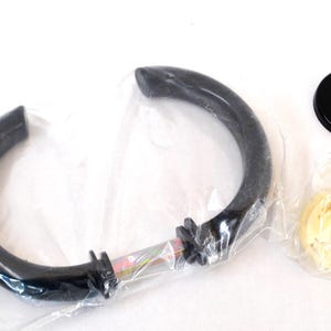 Puede incluir: Una manija de puerta de plástico negro con un tornillo plateado. La manija está empaquetada en una bolsa de plástico transparente con otros accesorios.