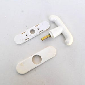 Può includere: Maniglia per porta in plastica bianca con un design a forma di T. La maniglia è smontata, mostrando le parti separate.