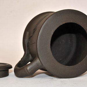 May include: A brown ceramic teapot with a lid and a spout. The teapot has a round body and a handle on the side. The teapot is sitting on a white surface.