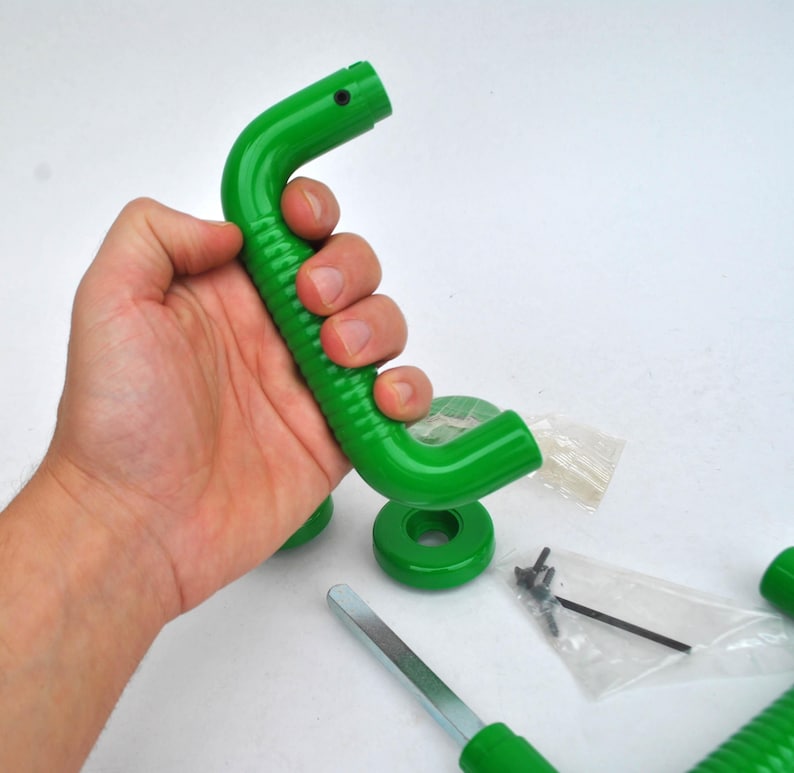 May include: A bright green, curved handle with a ridged grip, held in a hand. Additional green circular pieces, screws, and a metal tool are also visible, suggesting a construction or repair item.