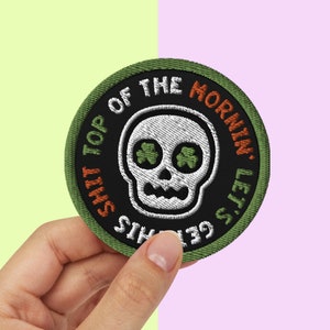 Op de afbeelding: Groen, oranje en wit geborduurd patch met een schedel met klaverbladogen en de tekst "This Shit Top of the Mornin', Let's Get This"