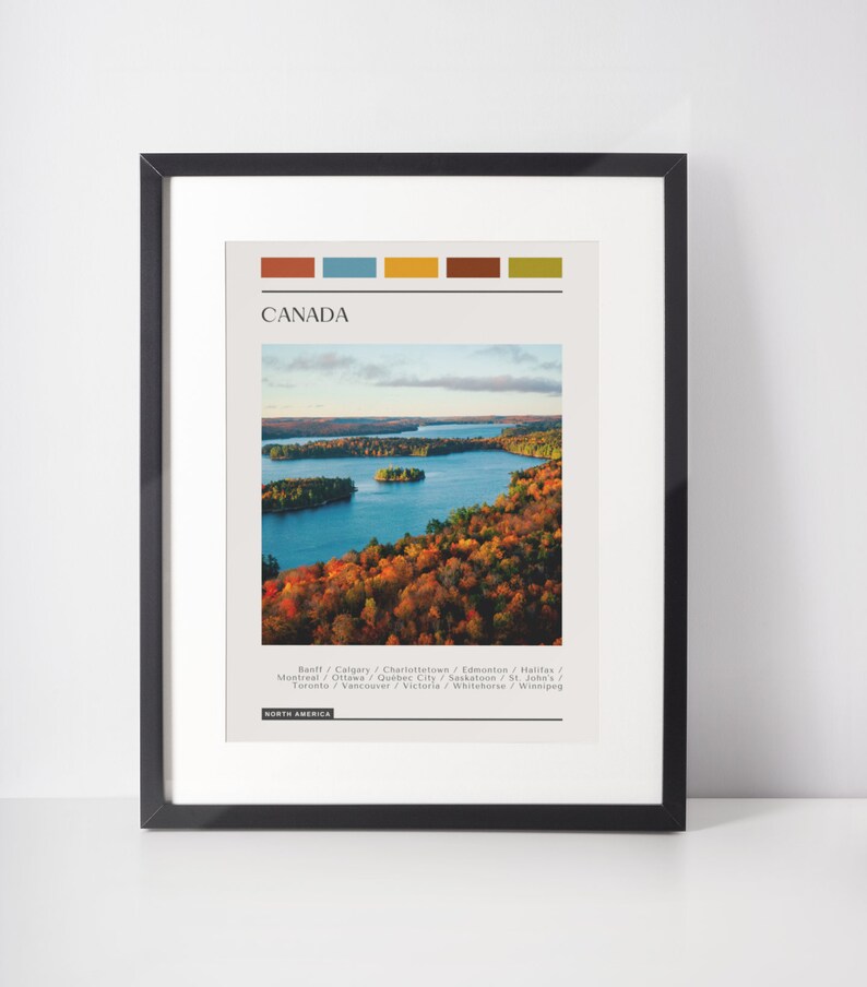 May include: A minimalist poster with a colorful stripe design at the top. The poster features a photograph of a lake surrounded by trees in autumn colors. The text "CANADA" is in a bold font at the top of the poster. Below the image, the text "Banff/Calgary/Charlottetown/Edmonton/Halifax/Montreal/Ottawa/Quebec City/Saskatoon/St. John's/Toronto/Vancouver/Victoria/Whitehorse/Winnipeg" is listed in a smaller font. The text "NORTH AMERICA" is at the bottom of the poster.