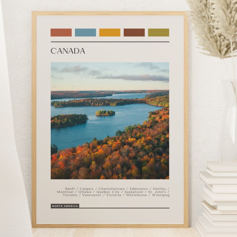 May include: A poster with a colorful palette of brown, blue, yellow, and green. The poster features a scenic aerial view of a lake surrounded by fall foliage. The text "CANADA" is at the top of the poster, and the text "NORTH AMERICA" is at the bottom. The poster lists the following cities: Banff, Calgary, Charlottetown, Edmonton, Halifax, Montreal, Ottawa, Quebec City, Saskatoon, St. John's, Toronto, Vancouver, Victoria, Whitehorse, and Winnipeg.