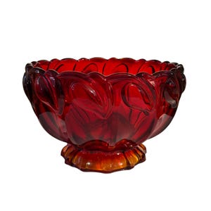 May include: A ruby red glass bowl with a decorative floral design. The bowl has a scalloped rim and sits on a pedestal base. The glass has a glossy finish and is transparent.