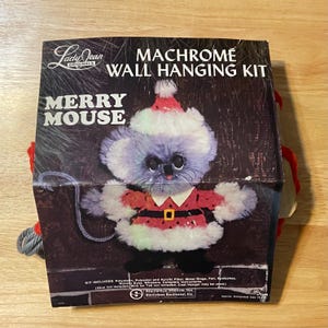May include: A vintage "Merry Mouse" Machrome wall hanging kit. The box features a whimsical, fluffy mouse wearing a Santa hat and coat. The kit includes materials like polyester, metal rings, and felt. The approximate completed size is 19 inches.