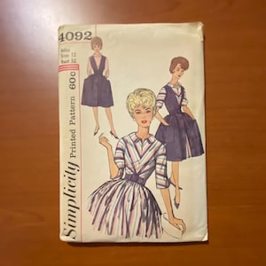 May include: Vintage Simplicity sewing pattern, featuring illustrations of women's dresses. The pattern cover displays the number 4092, with text indicating size 12 and bust 32. The cover has a retro aesthetic, with a color palette of white, pink, and navy.