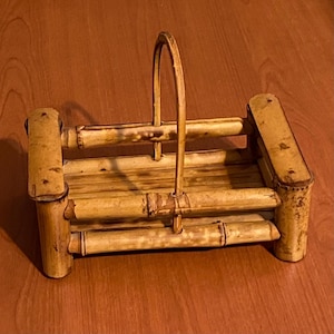 May include: A natural bamboo basket with a handle. The basket is rectangular with rounded corners and a handle that arches over the top. The bamboo has a light brown color with darker brown accents.