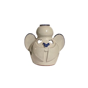 May include: Cream-colored ceramic angel figurine with blue accents. The angel has heart-shaped cutouts on the wings and face, and a blue bird-like design on the chest. The wings and head are outlined in blue.
