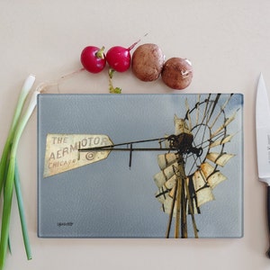 May include: A glass cutting board with a vintage image of a rusty windmill with a sign that reads "The Aermotor Chicago".