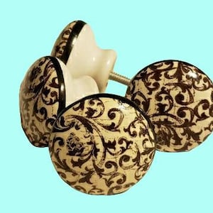 May include: Four ceramic cabinet knobs with a black and cream floral pattern. The knobs have a black trim around the edge.