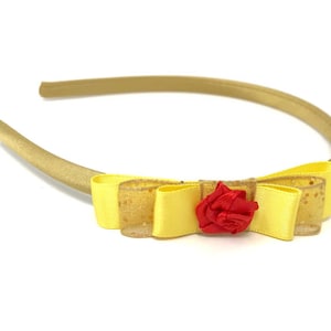 Puede incluir: Una diadema de satén amarilla con un lazo amarillo y un acento de rosa roja.