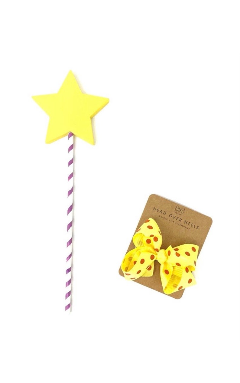 May include: A yellow star-shaped wand with a purple and white striped stick. A yellow bow with red polka dots is on a brown card with the text "Head Over Heels Boutique Hair Accessories".
