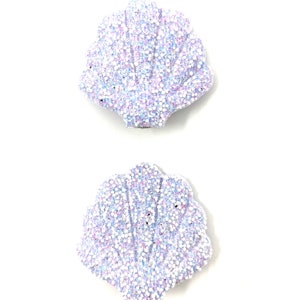 May include: Two iridescent white seashell-shaped hair clips with a glittery finish.