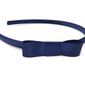 Op de afbeelding: Een marineblauw hoofdband met een satijnen strik. De hoofdband is gemaakt van zacht, flexibel materiaal en is perfect om elke outfit een vleugje elegantie te geven.