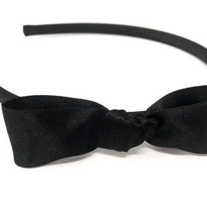 May include: A black headband with a black satin bow. The bow is tied in a knot in the centre.