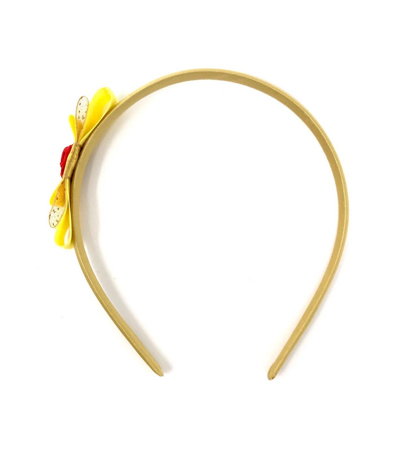 Puede incluir: Una diadema dorada con un adorno de flor amarilla y roja.