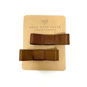 May include: Two brown satin hair bows on a brown card with the text "HEAD OVER HEELS UNIQUE HAIR ACCESSORIES".