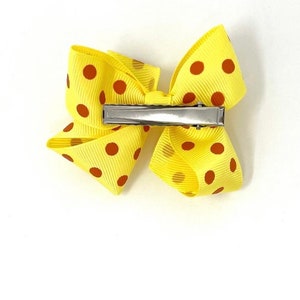 May include: A yellow bow with red polka dots and a silver alligator clip.
