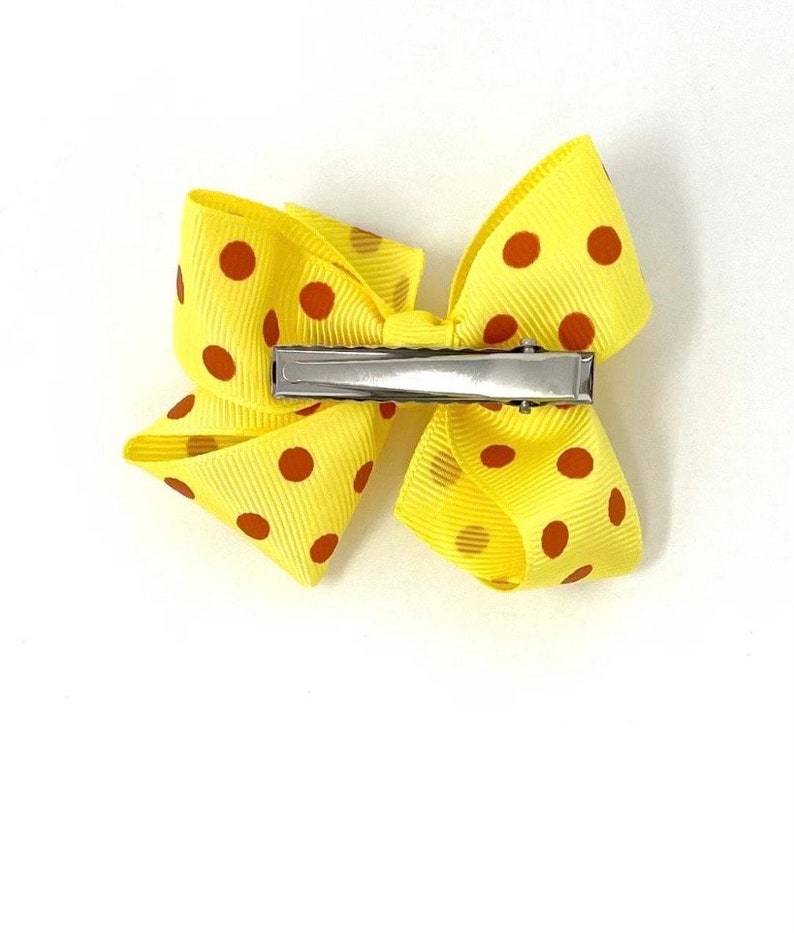 May include: A yellow bow with red polka dots and a silver alligator clip.