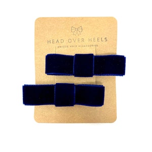 May include: Two navy blue velvet hair bows on a brown card with the text "HEAD OVER HEELS UNIQUE HAIR ACCESSORIES".