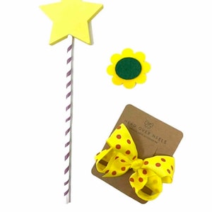 May include: A yellow star-shaped wand with a white and purple striped stick, a yellow felt sunflower with a green center, and a yellow bow with red polka dots on a brown card with the text "Head Over Heels" and "Unique Hair Accessories".