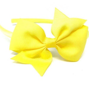 May include: A yellow headband with a large yellow bow. The headband is made of plastic and the bow is made of fabric.