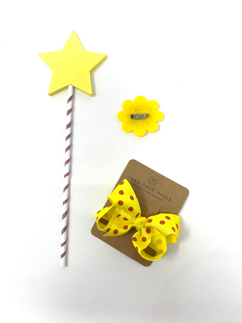 May include: Yellow star-shaped wooden wand with purple and white stripes, a yellow felt flower with a pin, and a yellow bow with brown polka dots on a brown card with the text "Head Over Heels Unique Hair Accessories".