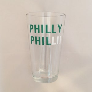 May include: A clear glass pint glass with the words "PHILLY PHILLY" printed in green and white.