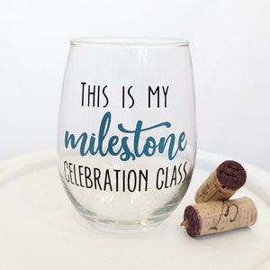 May include: A clear glass wine glass with the text "This is my milestone celebration glass" printed on it. The text is in black with a blue accent.