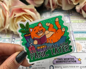 May include: A sticker with an orange cat reading a book, lying on a pillow, and a small potted plant. The sticker has the text "PROCRASTINATE NOW PANIC LATER" in white letters on a green background.