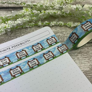 May include: A roll of washi tape with a repeating pattern of blue sky, white clouds, green grass, and brown wooden signs with positive affirmations. The signs say "You are amazing", "You are enough", "You are worthy", "You are talented", and "You are loved".