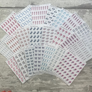 May include: A collection of 14 sheets of stickers featuring various designs, including hearts, butterflies, cats, and other abstract shapes. The stickers are printed on white paper with a glossy finish. The sheets are arranged in a fan shape on a wooden surface.