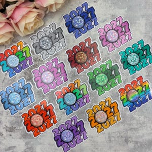 May include: A collection of stickers featuring the year 2027 in a bold, repeating font arranged in a circular pattern. Each sticker includes a central, circular disco ball graphic with various colours, including blue, pink, green, and orange.