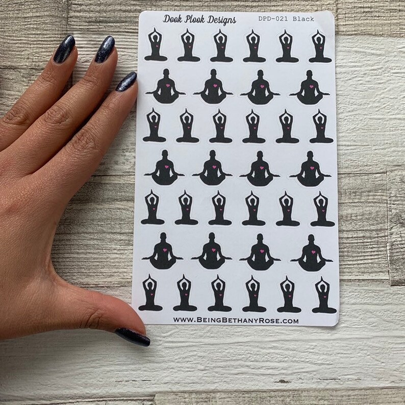 Op de afbeelding: Een vel met zwarte en witte yoga-pose stickers met een roze hart in het midden van elke pose. Het vel heeft de tekst "Dook Plook Designs" en "DPD-021 Black" bovenaan en "www.beingbethanyrose.com" onderaan.